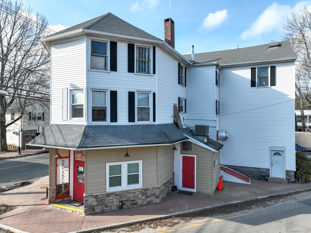 view of front of home featuring a shingled roof, a chimney, and central AC