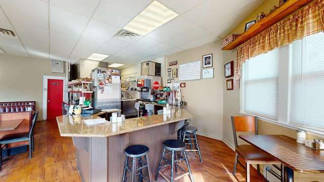 kitchen with freestanding refrigerator, a drop ceiling, visible vents, and wood finished floors