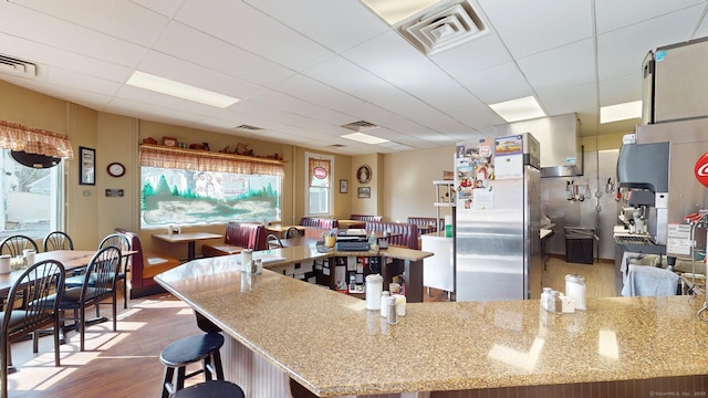 kitchen with light stone counters, stainless steel fridge, visible vents, and wood finished floors