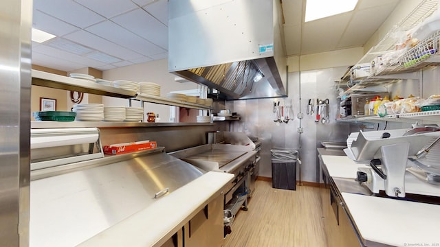 kitchen with a paneled ceiling, island range hood, stainless steel countertops, open shelves, and light wood finished floors