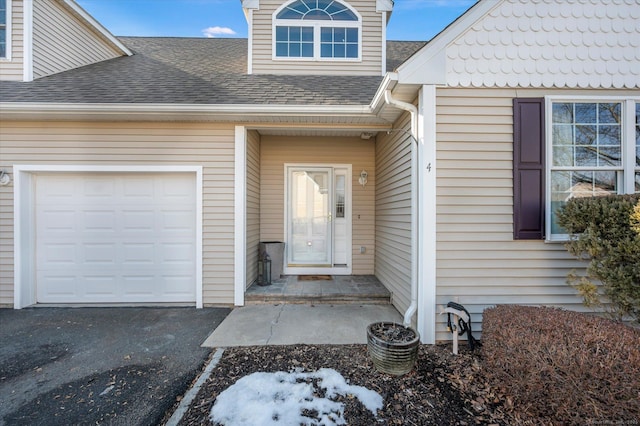 property entrance featuring aphalt driveway, roof with shingles, and an attached garage