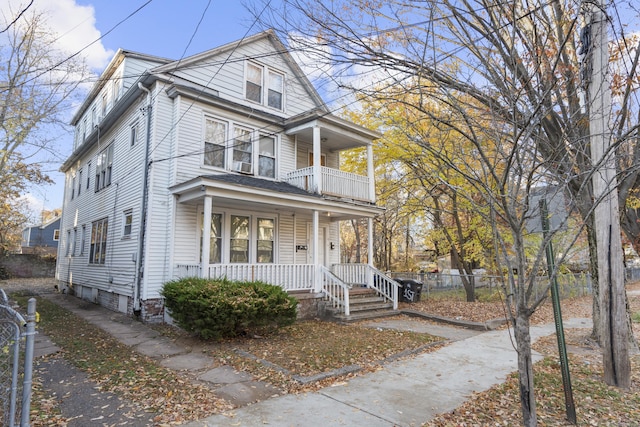 view of front facade featuring a balcony, covered porch, and fence