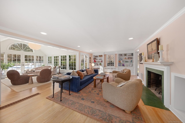 living room featuring built in features, wood finished floors, crown molding, french doors, and a fireplace