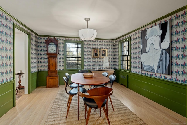 dining area featuring crown molding, wainscoting, wood finished floors, and wallpapered walls