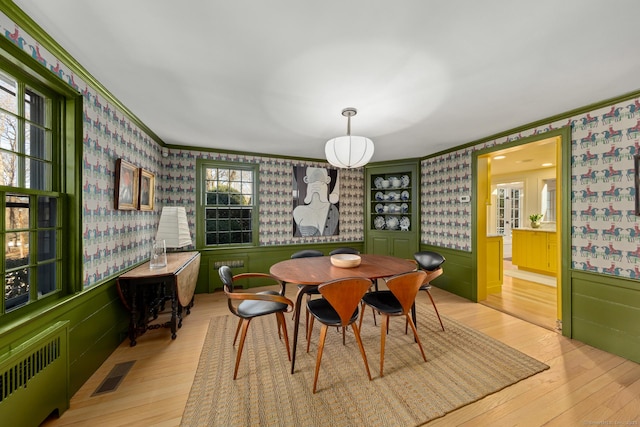 dining space with wallpapered walls, visible vents, wainscoting, radiator, and light wood-style flooring