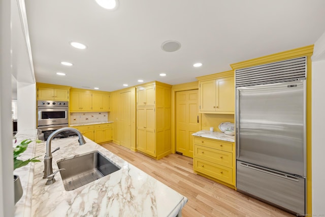 kitchen with appliances with stainless steel finishes, light wood-type flooring, a sink, and light stone counters