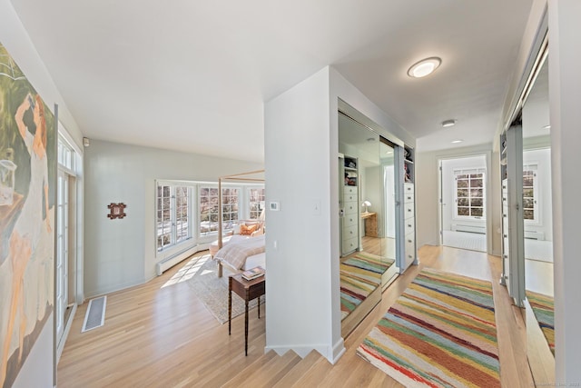 hallway featuring light wood finished floors, baseboard heating, visible vents, and baseboards