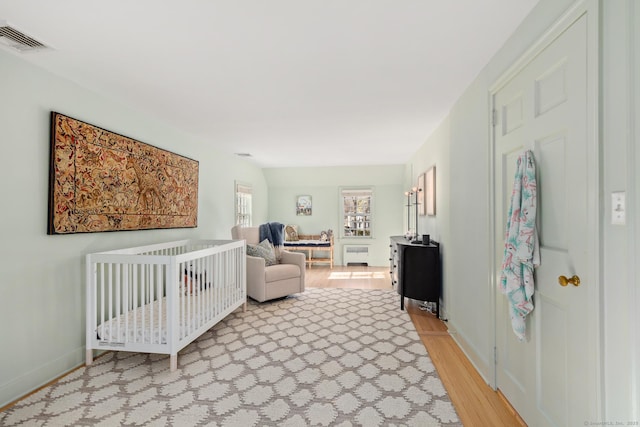 bedroom with light wood finished floors, baseboards, visible vents, radiator heating unit, and a nursery area