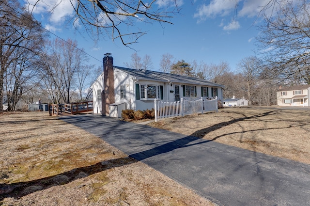 view of front of home featuring aphalt driveway, a chimney, and fence