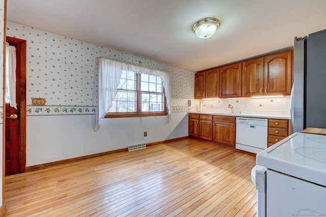 kitchen featuring brown cabinets, freestanding refrigerator, white dishwasher, wallpapered walls, and range