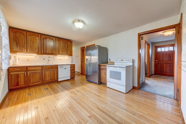 kitchen with light wood finished floors, tasteful backsplash, light countertops, brown cabinets, and white appliances