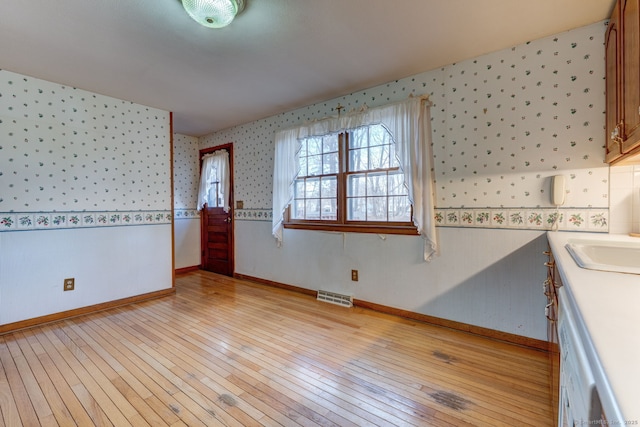 interior space with visible vents, light wood-style flooring, wallpapered walls, and baseboards