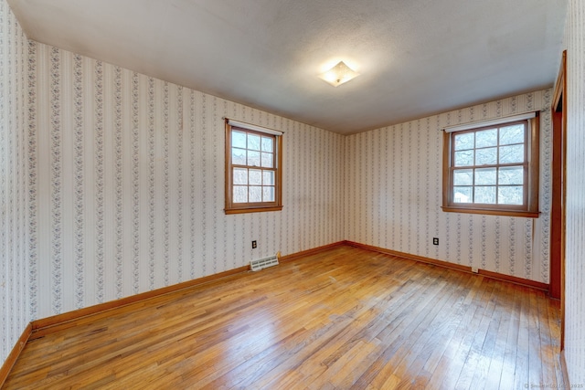 spare room with wallpapered walls, light wood-style flooring, visible vents, and a wealth of natural light