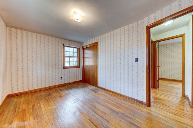 empty room featuring wallpapered walls, light wood-style floors, and baseboards