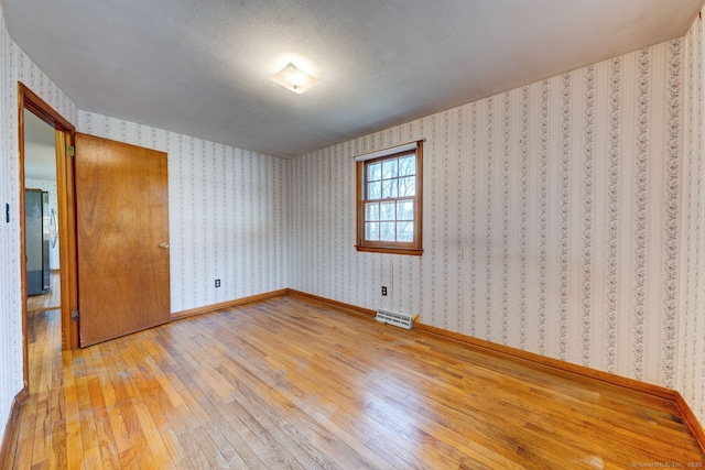 empty room featuring visible vents, light wood finished floors, baseboards, and wallpapered walls