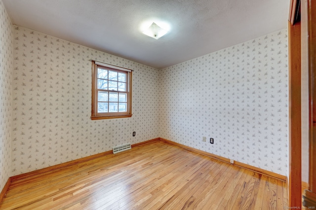 empty room with visible vents, light wood-style flooring, wallpapered walls, and baseboards