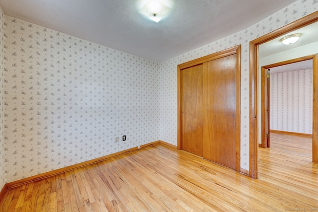 unfurnished bedroom with light wood-type flooring, baseboards, and wallpapered walls