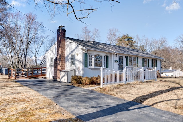 view of front of house with aphalt driveway, a chimney, and fence