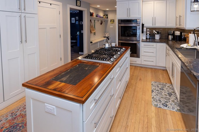 kitchen featuring white cabinets, appliances with stainless steel finishes, light wood-type flooring, wooden counters, and backsplash