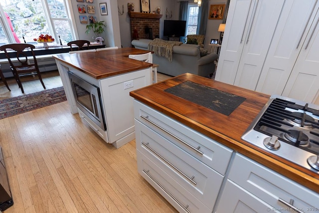 kitchen featuring a fireplace, butcher block counters, stainless steel gas stovetop, light wood-style floors, and plenty of natural light