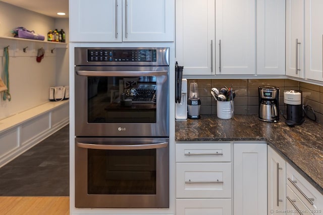 kitchen featuring double oven, dark stone counters, white cabinets, and tasteful backsplash