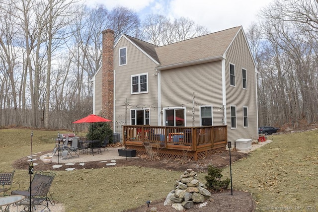 rear view of property featuring a patio, a chimney, a wooden deck, and roof with shingles