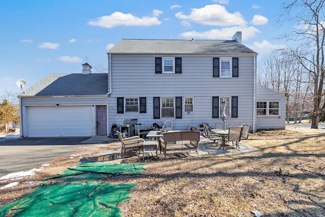 rear view of house with a garage, a patio area, driveway, and a chimney