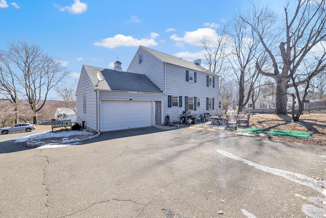 view of front of house with a garage, fence, driveway, roof with shingles, and a chimney