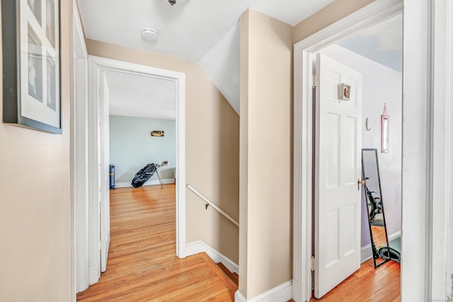 hallway with light wood finished floors, an upstairs landing, and baseboards