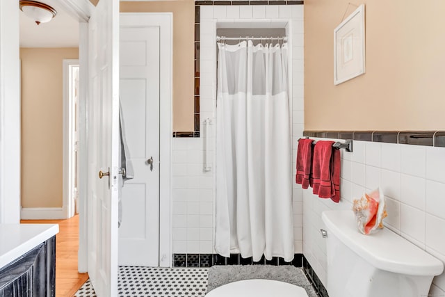 full bath featuring a shower with curtain, wainscoting, tile walls, and toilet