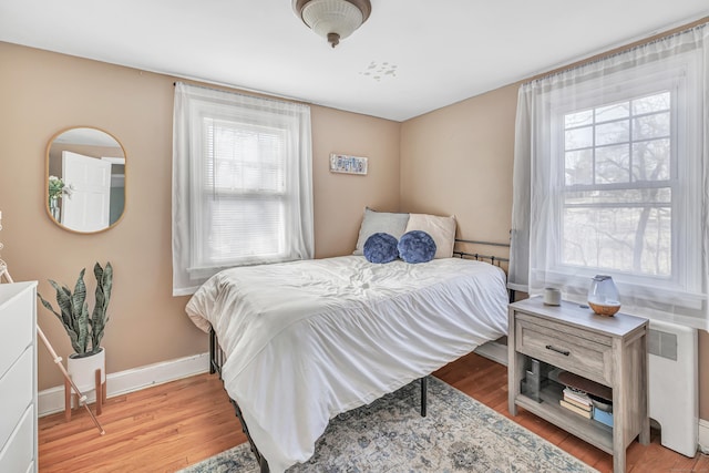 bedroom featuring radiator heating unit, baseboards, and light wood finished floors