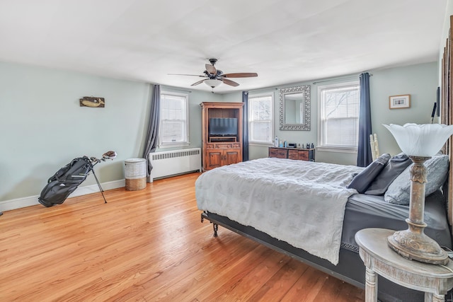 bedroom with light wood-style floors, radiator heating unit, baseboards, and ceiling fan