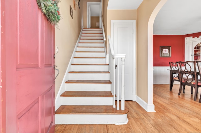 stairs featuring arched walkways, wood finished floors, and baseboards