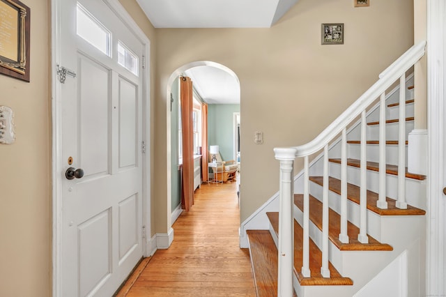 foyer entrance with light wood-type flooring, arched walkways, stairway, and baseboards