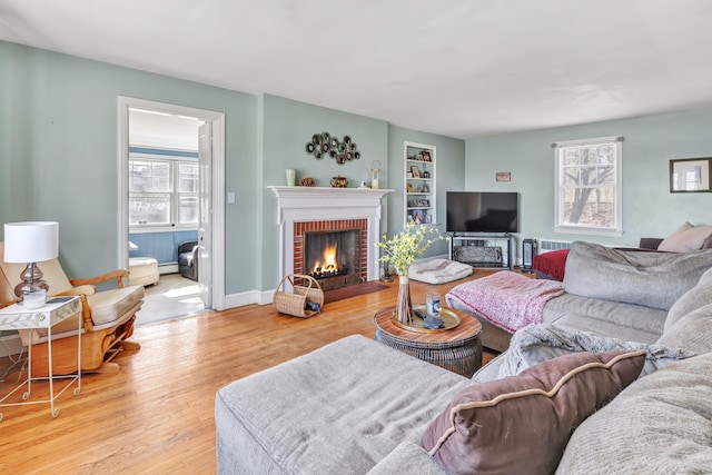 living area with a brick fireplace, built in features, a wealth of natural light, and wood finished floors