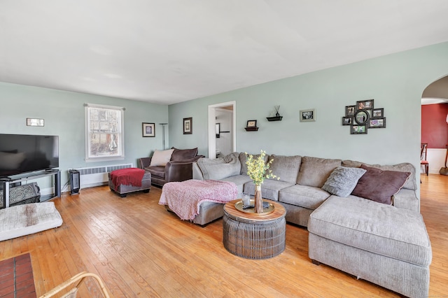 living area featuring arched walkways, wood-type flooring, and radiator heating unit