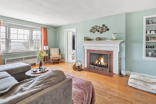 living room with radiator heating unit, a fireplace, baseboards, and wood finished floors