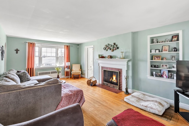 living room featuring built in shelves, baseboards, a fireplace, and wood finished floors