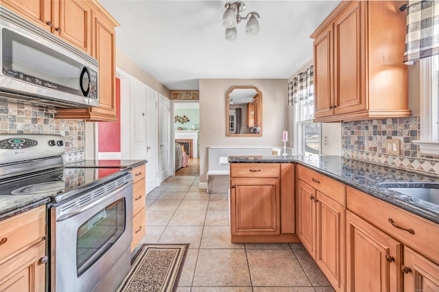 kitchen with light tile patterned floors, stainless steel appliances, dark stone counters, and a fireplace