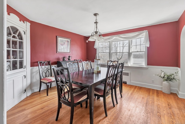 dining room featuring baseboards, light wood-style flooring, radiator heating unit, and an inviting chandelier