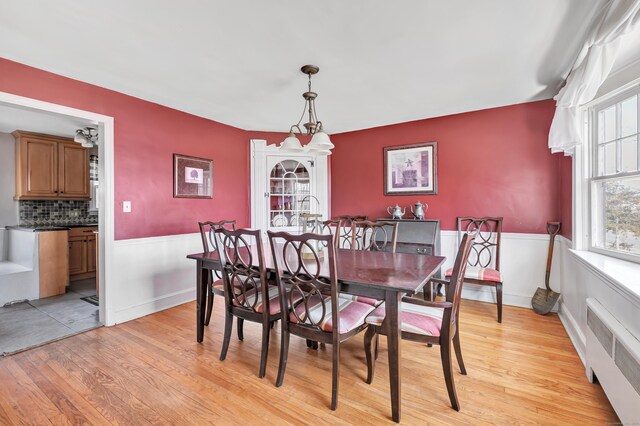 dining space featuring light wood-style floors, a wainscoted wall, and radiator heating unit