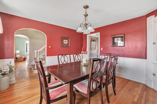 dining area featuring light wood-style floors, arched walkways, a chandelier, and stairs