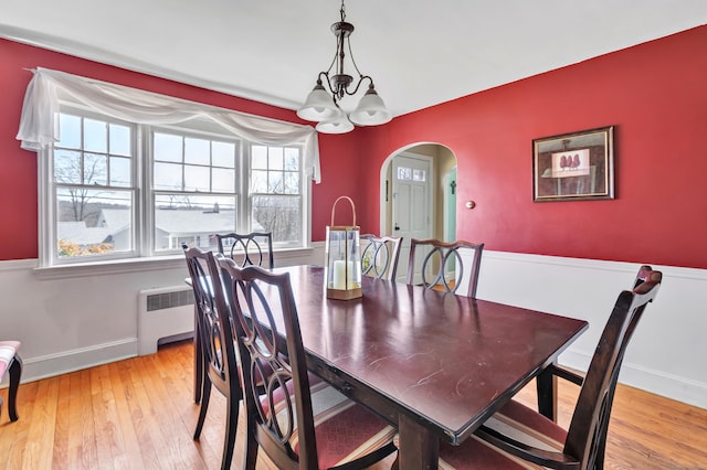 dining area with arched walkways, a notable chandelier, radiator heating unit, light wood-style floors, and baseboards