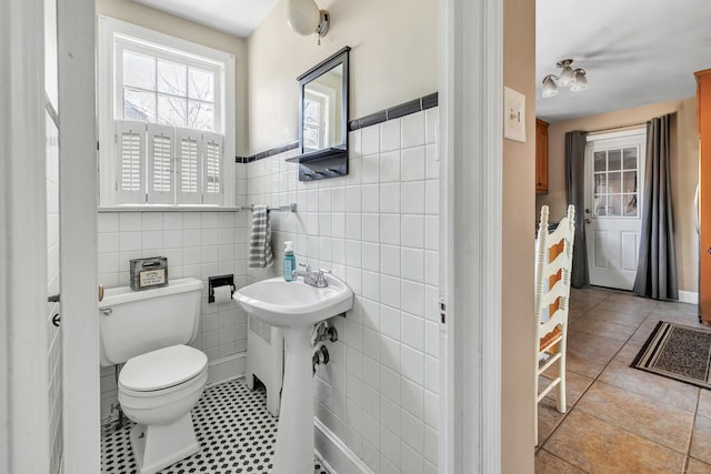 half bath featuring a wainscoted wall, tile patterned flooring, toilet, and tile walls