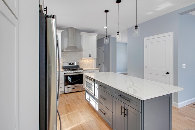 kitchen featuring stainless steel appliances, gray cabinets, backsplash, wall chimney range hood, and light wood-type flooring