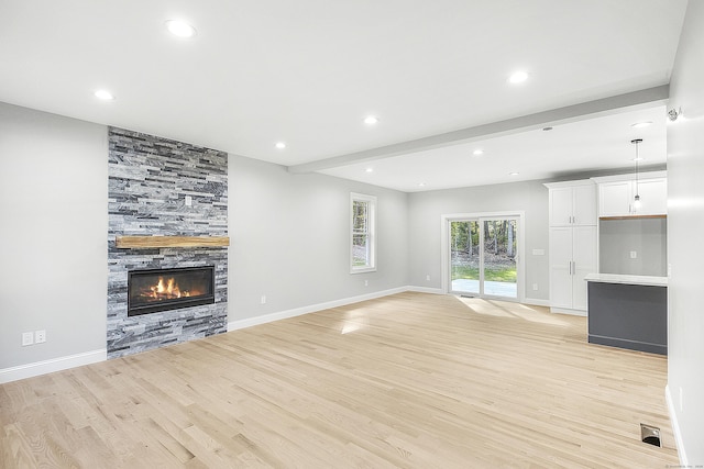 unfurnished living room featuring light wood-style flooring, baseboards, beamed ceiling, and a stone fireplace