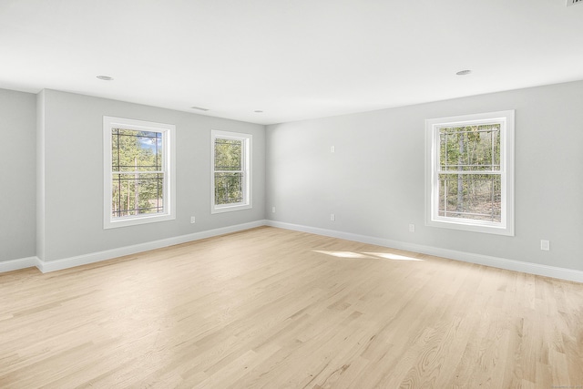 spare room with baseboards, a wealth of natural light, and light wood-style floors