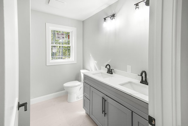 bathroom featuring baseboards, a sink, toilet, and double vanity