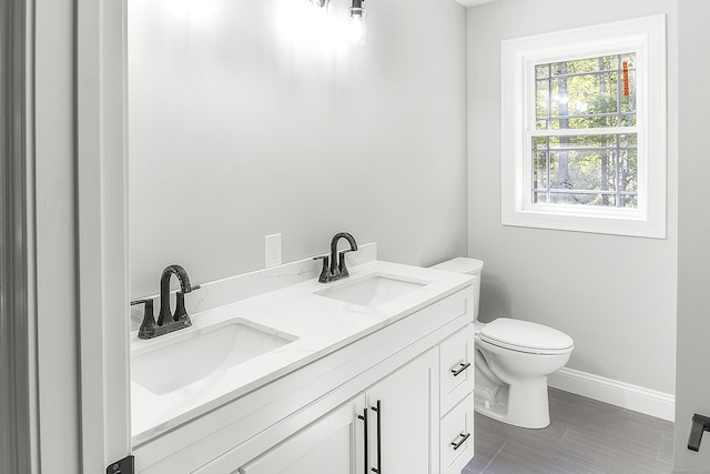 bathroom featuring toilet, double vanity, baseboards, and a sink