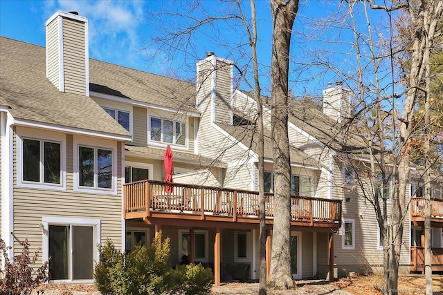 back of property with a shingled roof and a chimney